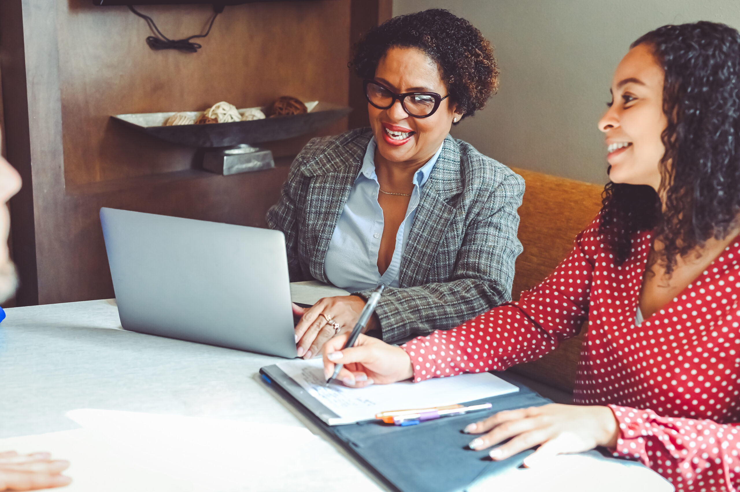 Two women sitting at a table with a laptop discussing tax documents.